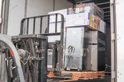 Forklift moving a large appliance, possibly a refrigerator, on a pallet.
